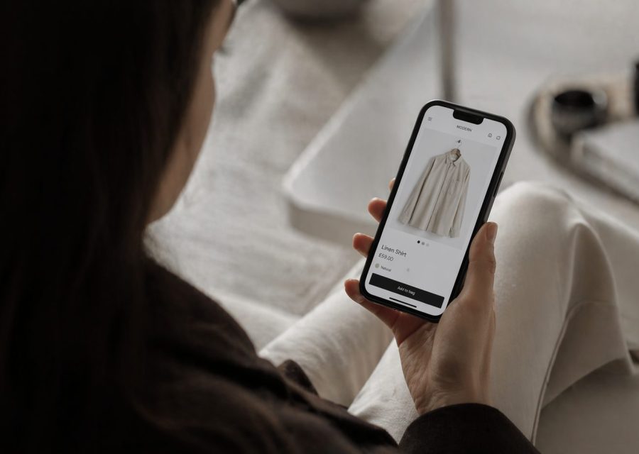 Person holding a smartphone displaying an online clothing product page for a linen shirt.