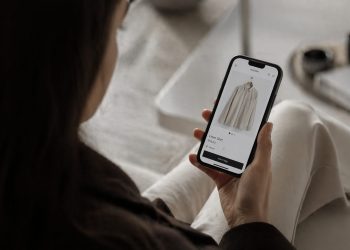 Person holding a smartphone displaying an online clothing product page for a linen shirt.