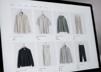 Laptop screen showing an online clothing store with a grid of six product photos (shirts, hoodie, pants) in neutral tones