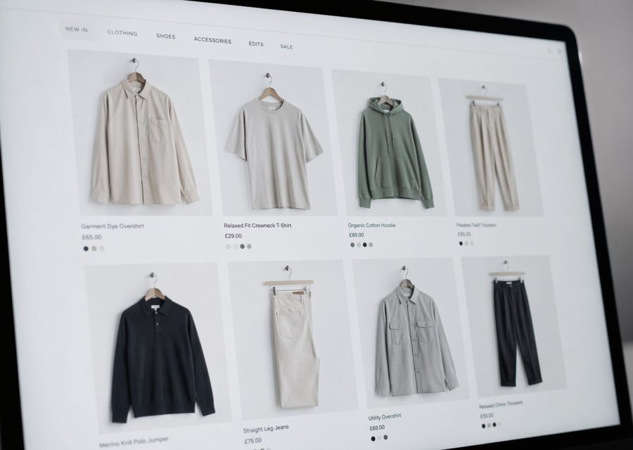 Online clothing store grid displaying six apparel items (shirts, hoodie, pants) on a laptop screen.